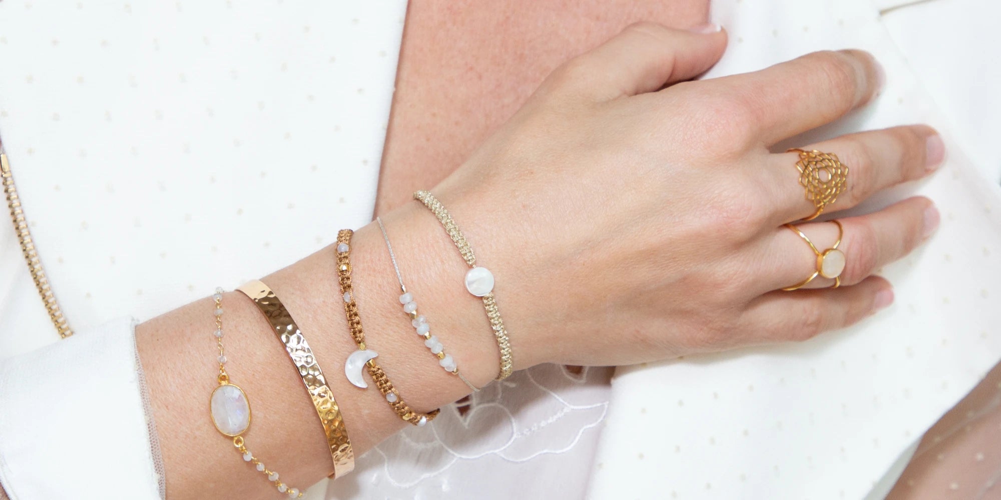 Detailaufnahme eleganter Amorlune Armbänder und goldener Ringe mit Edelsteinen am Handgelenk – stilvoller Schmuck als Geschenkidee für Frauen