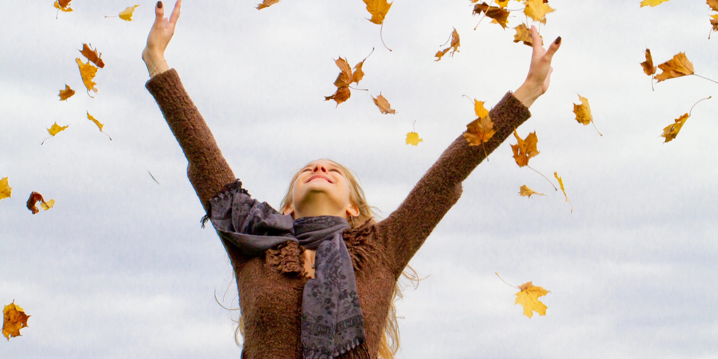 Glückliche Frau wirft Herbstblätter in die Luft und genießt den Moment – Symbol für Lebensfreude, Freiheit und besondere Augenblicke
