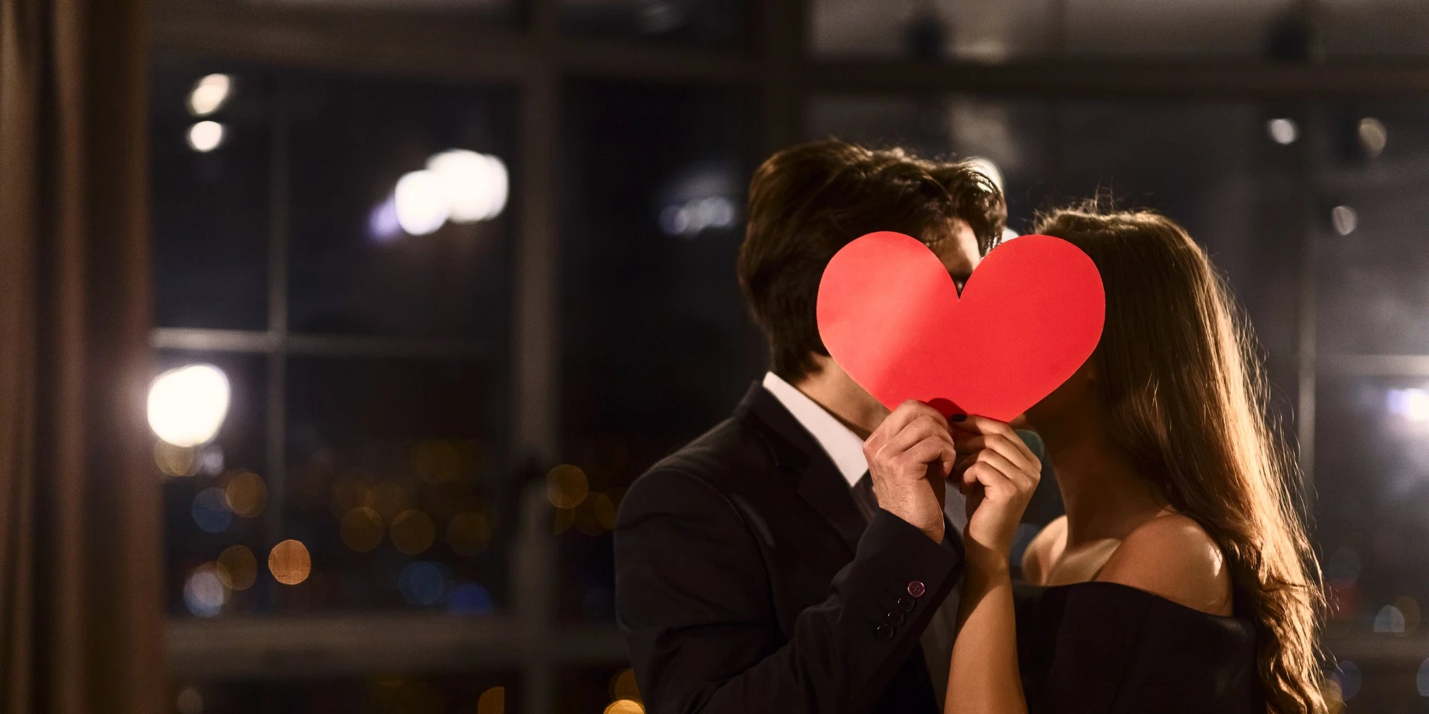 Verliebtes Paar im Abendlicht hält rotes Herz vor dem Gesicht – romantische Stimmung, perfekte Symbolik für Valentinstag, Liebe und besondere Geschenkideen für Paare von Amorlune